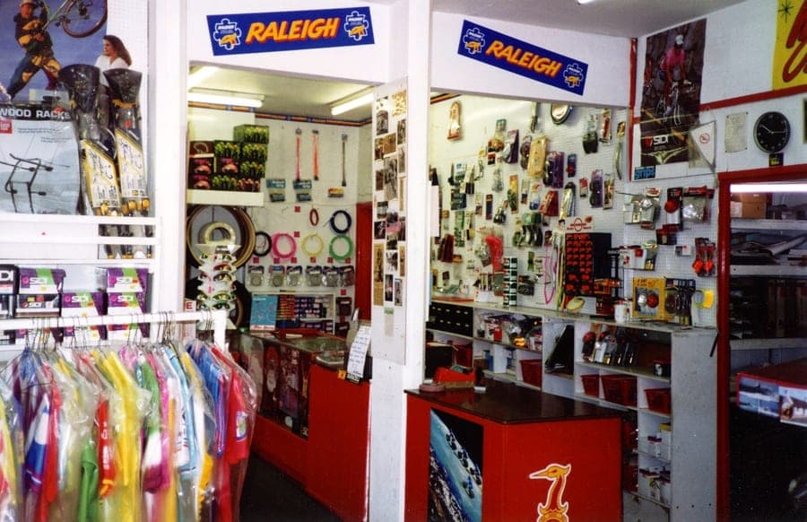 Shop interior with Raleigh banners over the doorway, racks of small parts on the walls and clothing on a rail.
