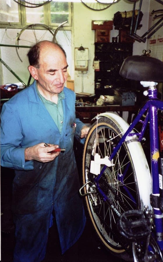 Sid in a blue coat working on the rear mech of a purple bicycle.