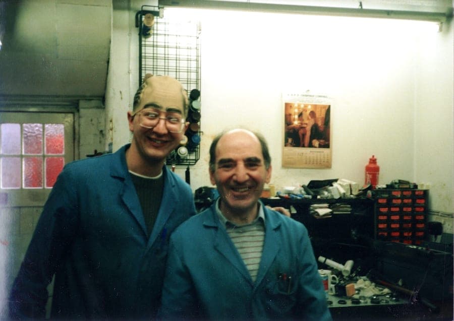 Kevin and Sid side by side in blue workshop coats at the back of the shop, both grinning at the camera.