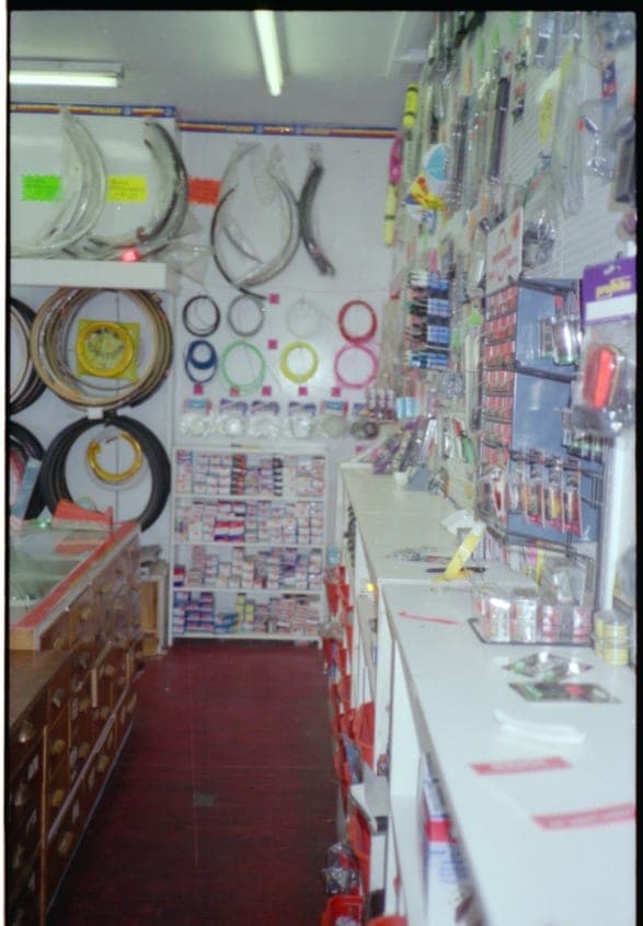 The shop interior with cables and small parts hung on a white pegboard wall, a red floor, and a glass counter along the right.