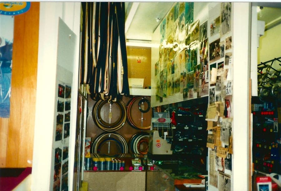Shop interior. Rims stacked along the wall, tubular tyres hanging in loops from the ceiling, a wall of photographs behind the counter.