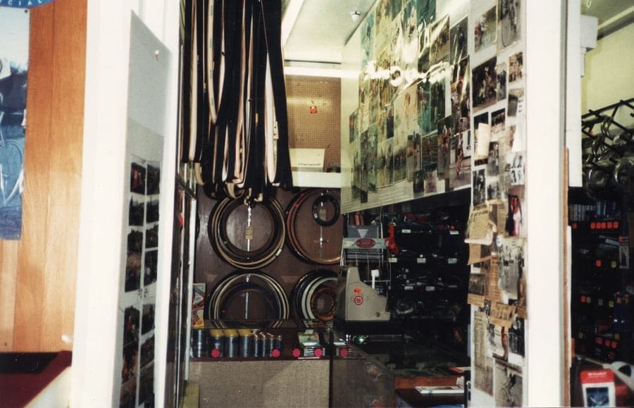 The inside of the shop, tyres hanging in bunches from the ceiling and tubular tyres coiled on the wall, with posters and boxed parts along the back.